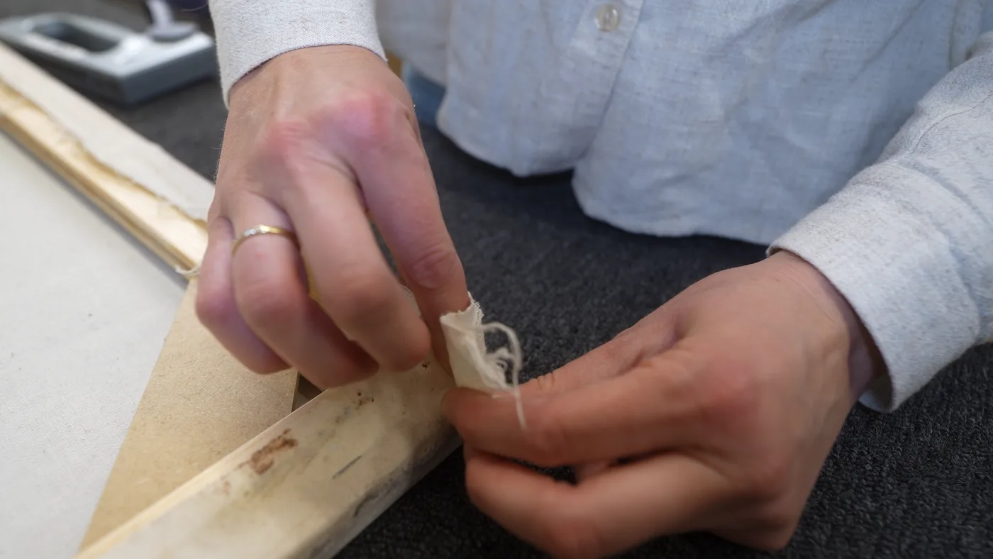 Handen vouwen het overtollige doek plat in de hoek van het spieraam