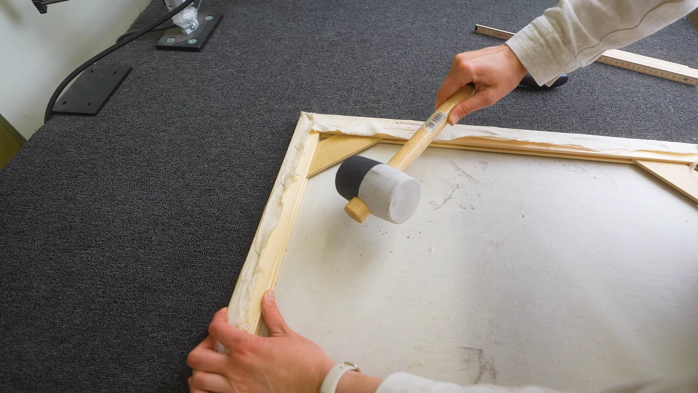 Een spie wordt met de houten hamer in de hoekgroef van het spieraam getikt