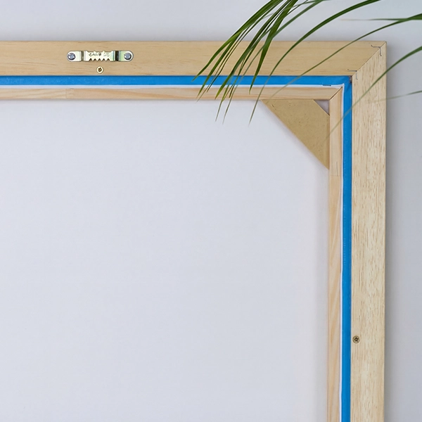 Achterkant van een baklijst met zaagtandophanger en canvas voor een lichtbeige muur. Een palmblad steekt in de afbeelding.